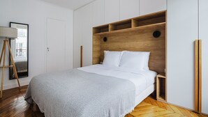 A bedroom with a wooden headboard, white bedding, and a herringbone-patterned rug. - Blueground | Notre-Dame-de-Lorette 1bd apartment (Paris)