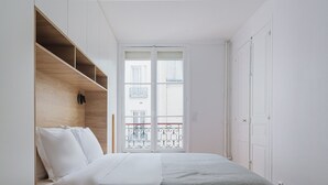 A bedroom with a bed, a wardrobe, and a window with a balcony. - Blueground | Notre-Dame-de-Lorette 1bd apartment (Paris)