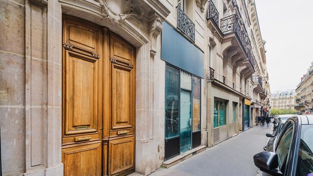 A street with a large wooden double door, a modern glass storefront, and a parked car. - Blueground | Notre-Dame-de-Lorette 1bd apartment (Paris)
