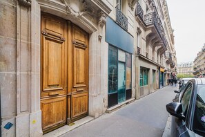 A street with a large wooden double door, a modern glass storefront, and a parked car. - Blueground | Notre-Dame-de-Lorette 1bd apartment (Paris)