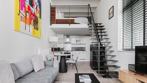 Un apartamento moderno con un sofá gris, una mesa de centro negra, una cocina, una escalera y un televisor.