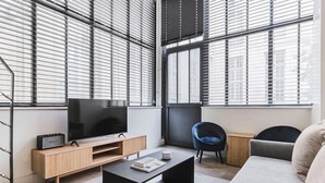 Una sala de estar moderna con un televisor sobre un mueble de madera, una mesa de centro negra, una silla azul y un sofá gris.