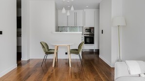 Une cuisine moderne avec des meubles blancs, un plan de travail blanc et des appareils en acier inoxydable. On y trouve une table de salle à manger ronde, accompagnée de deux chaises.