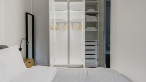 Une chambre à coucher comprenant un lit, une table de chevet, une armoire avec des vêtements suspendus et un miroir.