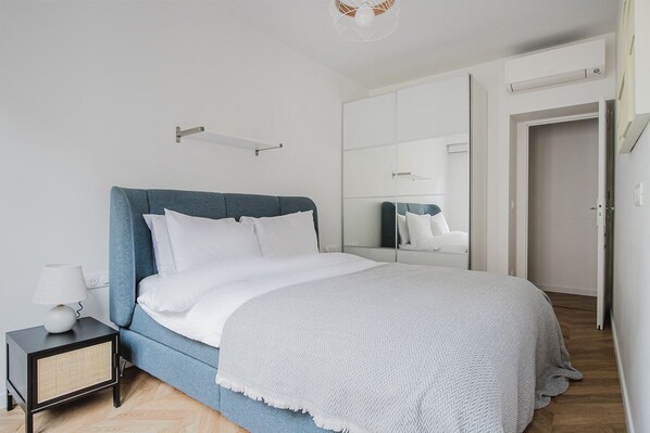 Une chambre à coucher moderne avec un lit, une table de chevet, une lampe et un grand miroir.