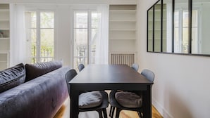 A modern living room with a dark wooden dining table, grey sofa, and large windows. - Blueground | Le Marais, elevator & w/d, nr Seine (Paris)