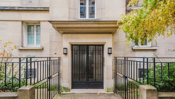 A townhouse with a black metal gate, a stone facade, and a small window above the door. - Blueground | Le Marais, elevator & w/d, nr Seine (Paris)