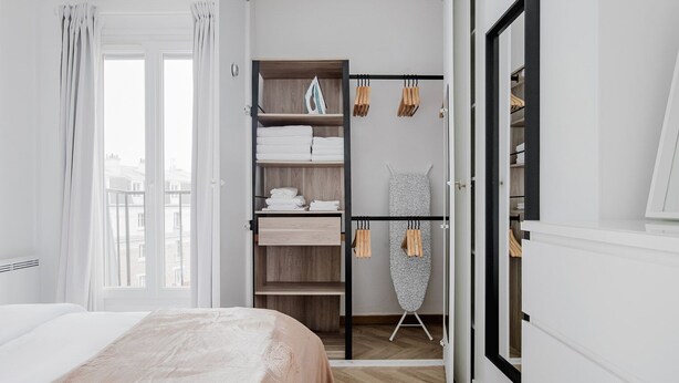 Un dormitorio con una cama, un armario con estantes y una tabla de planchar.