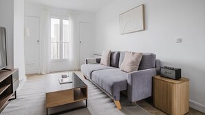 Una sala de estar moderna con un sofá gris, una mesita de madera, una mesa de centro de vidrio y un televisor sobre un mueble de madera.