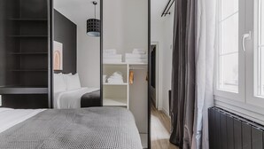 A modern hotel room with a bed, a wardrobe, a walk-in closet, and a window with curtains. - Blueground | Odéon, washer, nr Luxembourg Gdns (Paris)