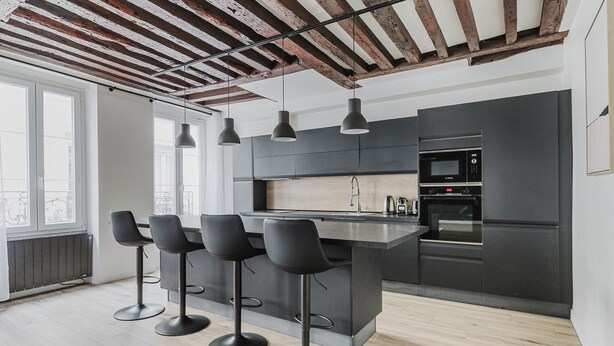 A modern kitchen with a central island, bar stools, and built-in appliances. - Blueground | Odéon, washer, nr Luxembourg Gdns (Paris)