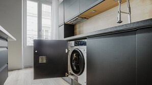 A modern kitchen with a built-in washer and dryer, a wooden countertop, and a large window providing natural light. - Blueground | Odéon, washer, nr Luxembourg Gdns (Paris)