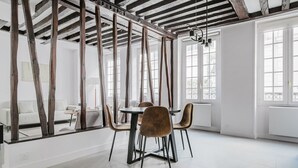 A dining area with a white table and chairs, exposed wooden beams, and large windows.