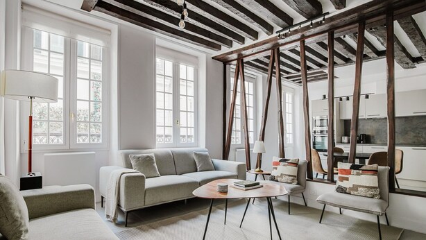 A modern living room with a sofa, armchairs, a coffee table, and a kitchen area visible through an open door.