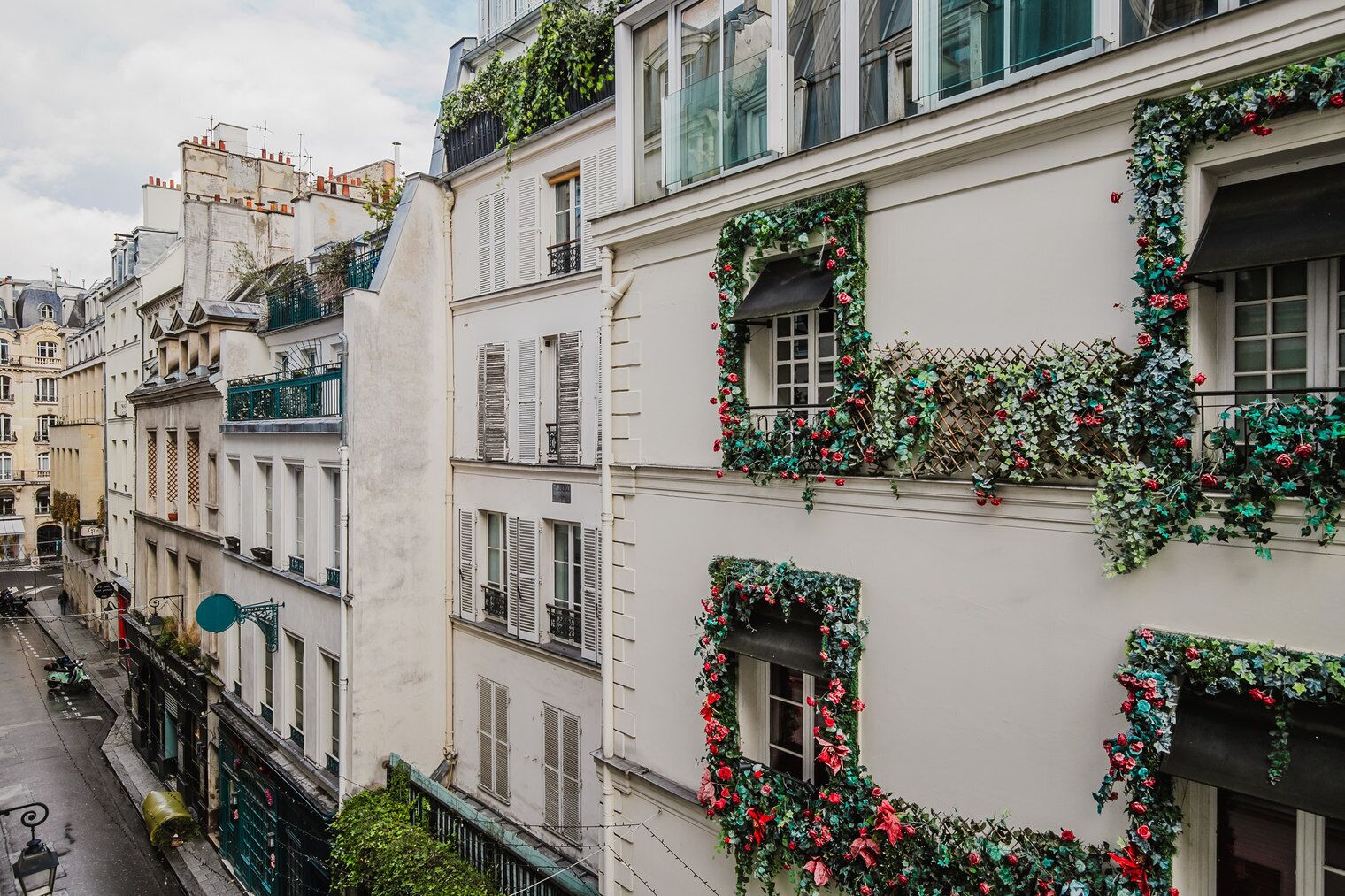 Una hilera de edificios blancos con contraventanas verdes y balcones decorados con flores rojas.
