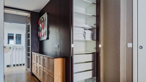 A hallway with a wooden cabinet, a wall-mounted picture, and a white shelving unit with towels. - Blueground | Le Marais, elevator & w/d, nr Vosges (Paris)