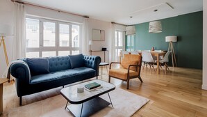 A modern living room with a blue sofa, a wooden coffee table, and a dining area with chairs and a table. - Blueground | Le Marais, elevator & w/d, nr Vosges (Paris)