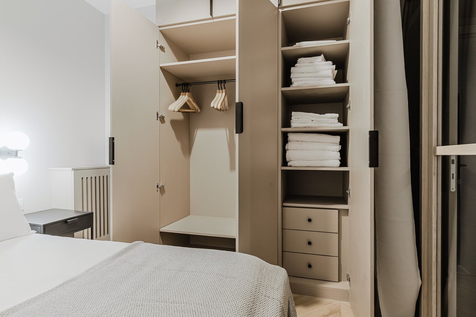 Ein Schlafzimmer mit Bett, Nachttisch, Kleiderschrank mit Kleiderstange und Regalen mit gefalteten Handtüchern.