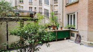 A courtyard with potted plants, a green door, and a brick building in the background. - Blueground | Auteuil, washer, nr Monceau Park (Paris)
