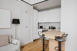 Kitchen features a microwave, kettle, and coffee maker on the countertop, adjacent to a cozy seating area with a sofa and floor lamp.