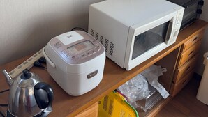 Ett köksutrymme med en mikrovågsugn, en riskokare och en vattenkokare placerade på en bänkskiva i trä.