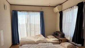 Ett hotellrum med tre sängar, ett trägolv, en takfläkt och ett fönster med gardiner.