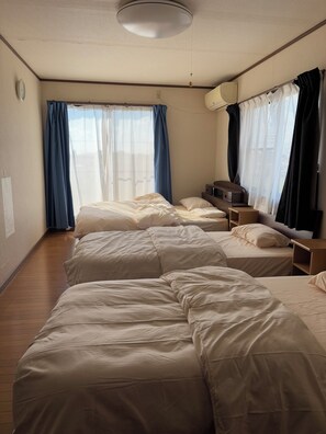 Three beds with white mattresses and pillows, a television, and a nightstand are featured in this hotel room.