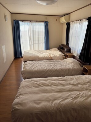 Two beds with white bedding, a nightstand, and a large window with sheer curtains.