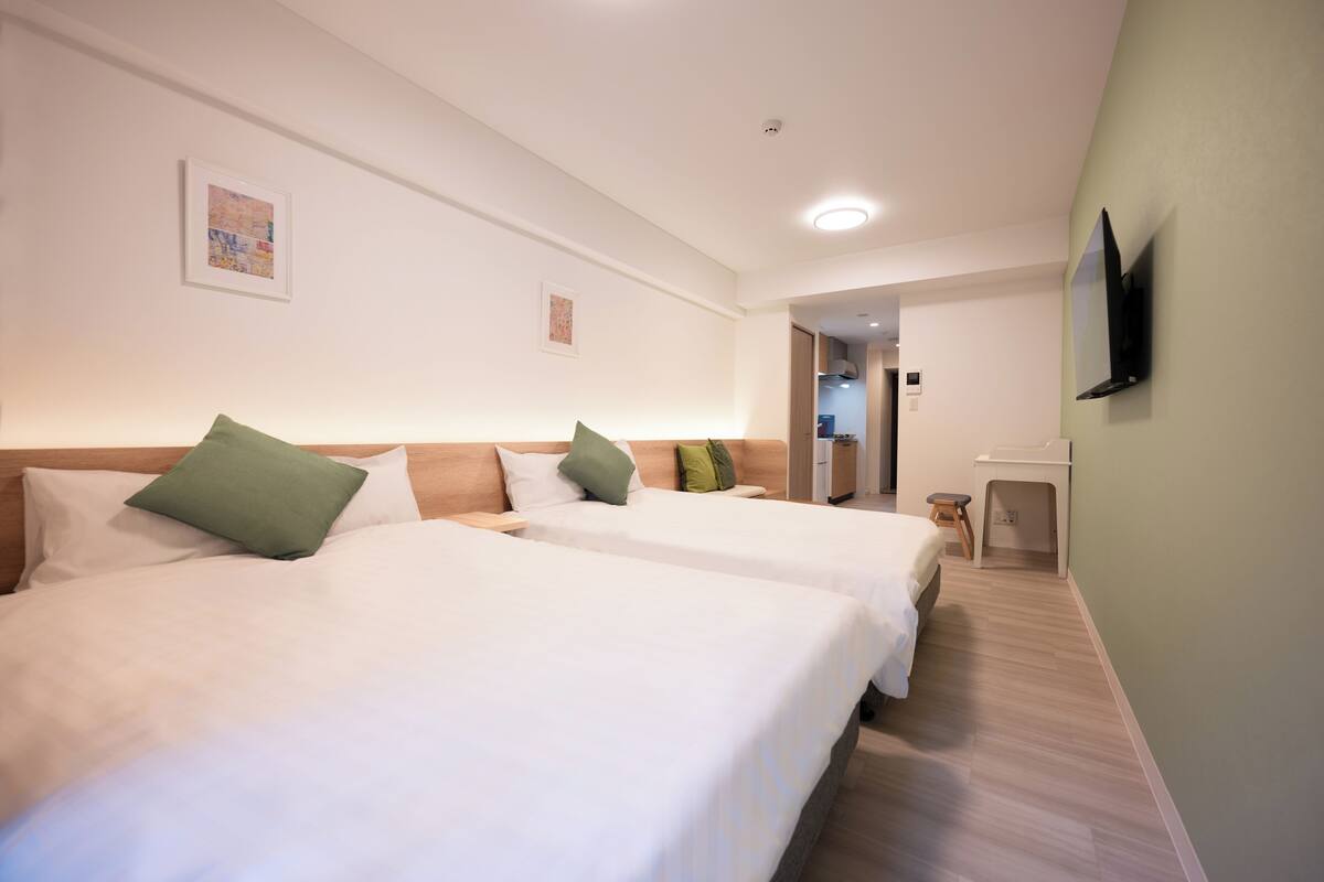 A hotel room with two beds, a TV mounted on the wall, and a small stool near the entrance.