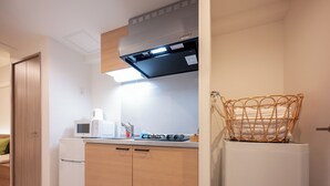 Egy praktikus, kis méretű konyha, amelyben van mikrohullámú sütő, egy kis hűtőszekrény, fa szekrények, és a hűtőszekrény tetején egy fonott kosár.