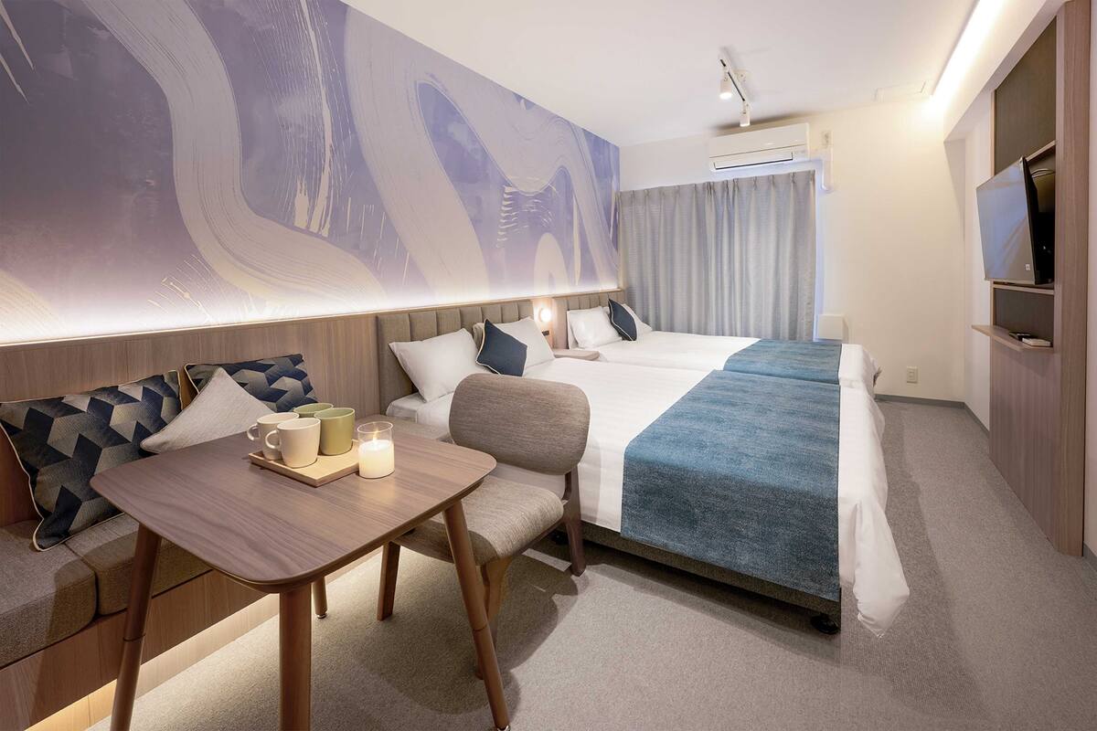 A hotel room with a bed, a desk, a chair, a TV, and a large abstract painting on the wall.