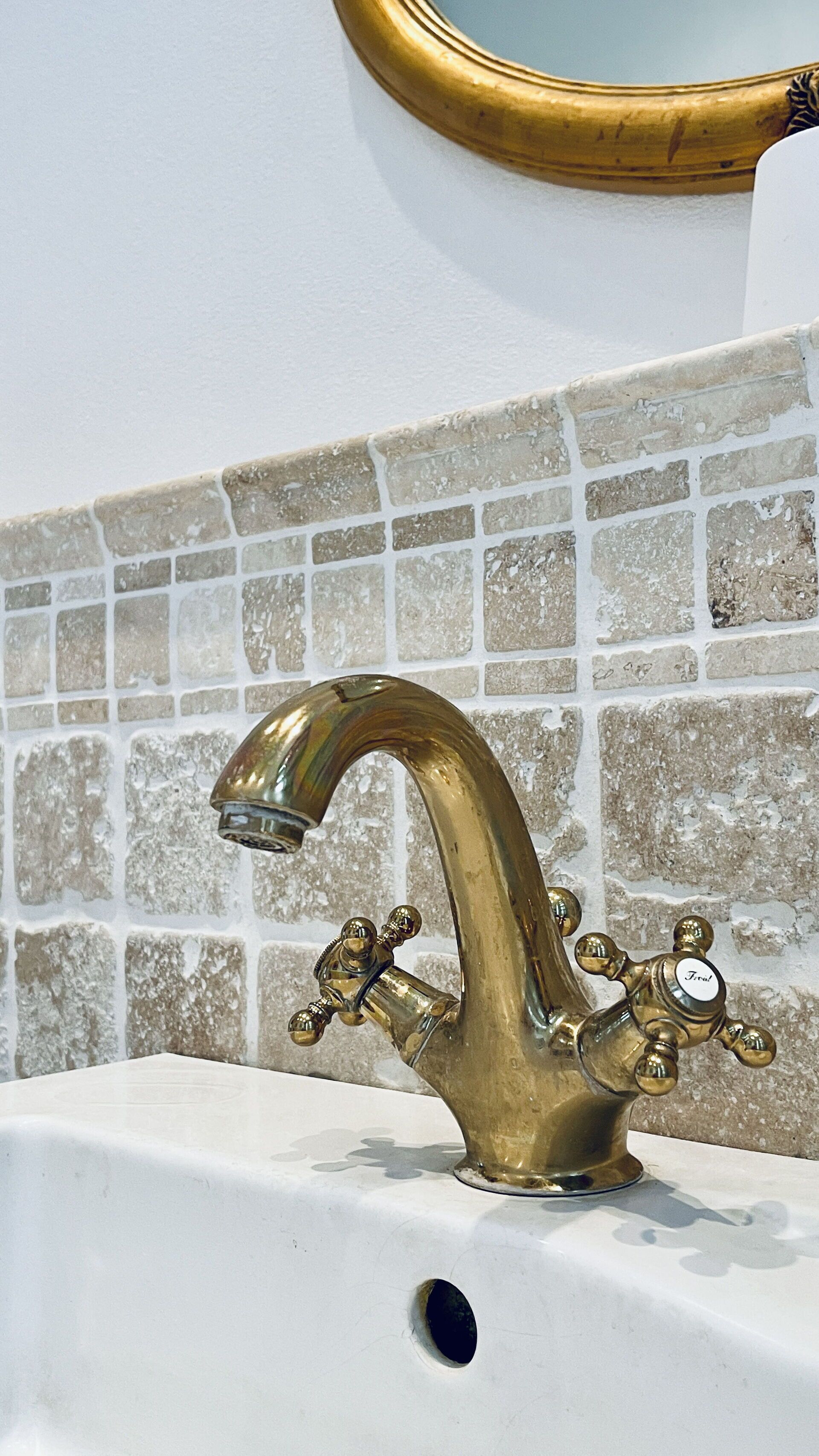 A bathroom with a gold faucet, a mirror, and a tiled backsplash.