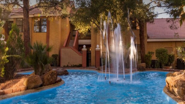 Una piscina con numerosi getti d'acqua, circondata da rocce e palme, con un edificio sullo sfondo.
