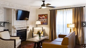 Una camera d'hotel con camino, una TV a schermo piatto posizionata sopra, un divano, un tavolino da caffè e una ventola a soffitto.