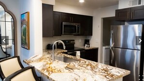 Una cucina moderna con mobili scuri, elettrodomestici in acciaio inossidabile, un piano di lavoro in marmo e un lavello.