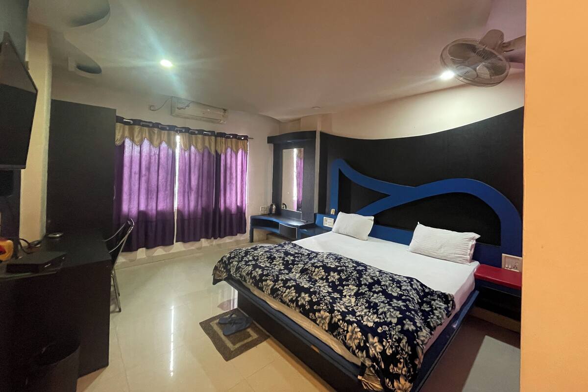 A bedroom with a bed, a desk, a chair, a mirror, and a ceiling fan.