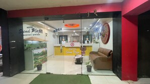 A hotel reception area with a glass door, a reception desk, a brown leather sofa, and a green mat on the floor.