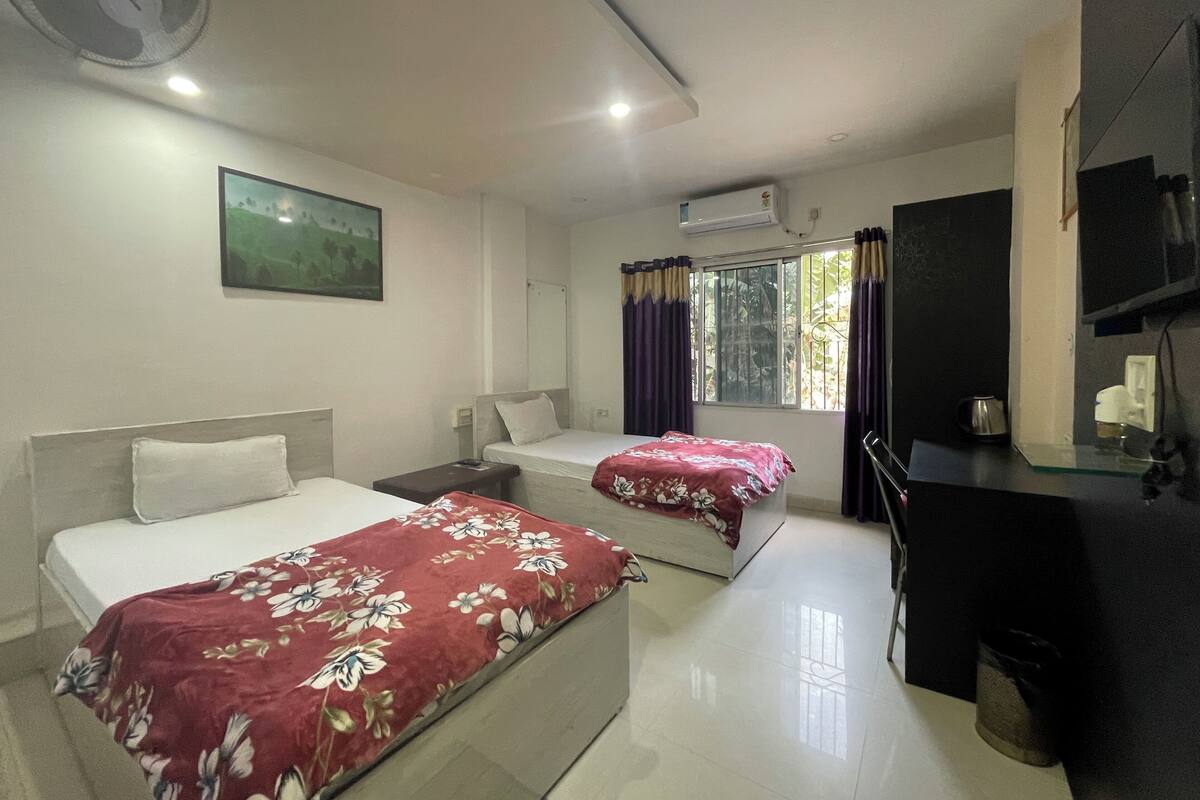 A hotel room with two beds, a desk, a chair, a TV, and a window with curtains.