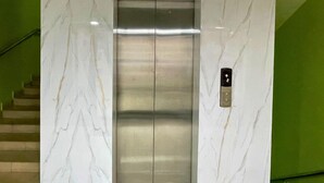An elevator with a marble wall and a green staircase.
