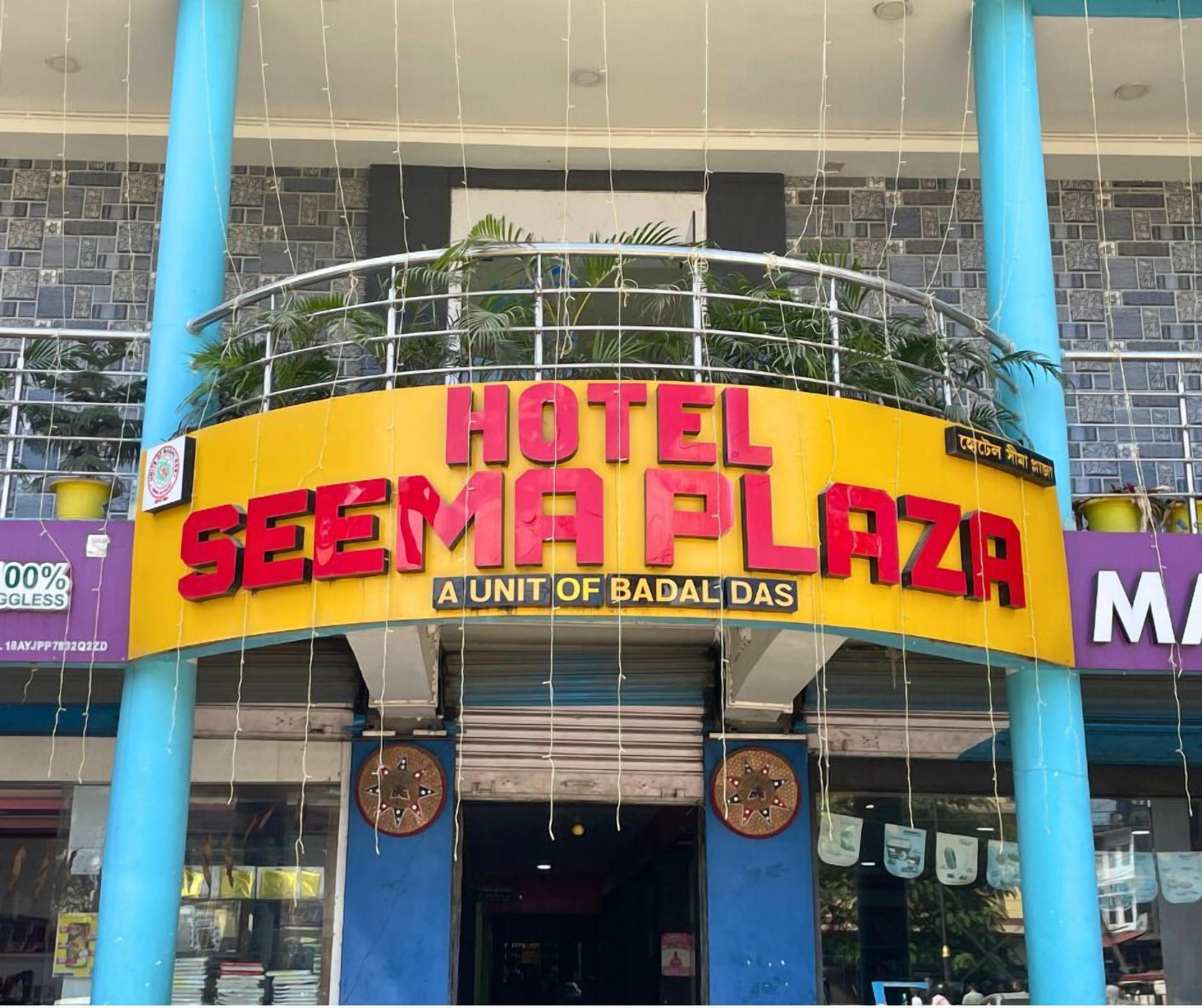 Exterior do Hotel Seema Plaza, com uma placa amarela e vermelha em destaque, exibindo o nome do hotel e um slogan.