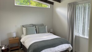 Un dormitorio con cama, mesita de noche, ventana con cortinas y techo con vigas de madera.