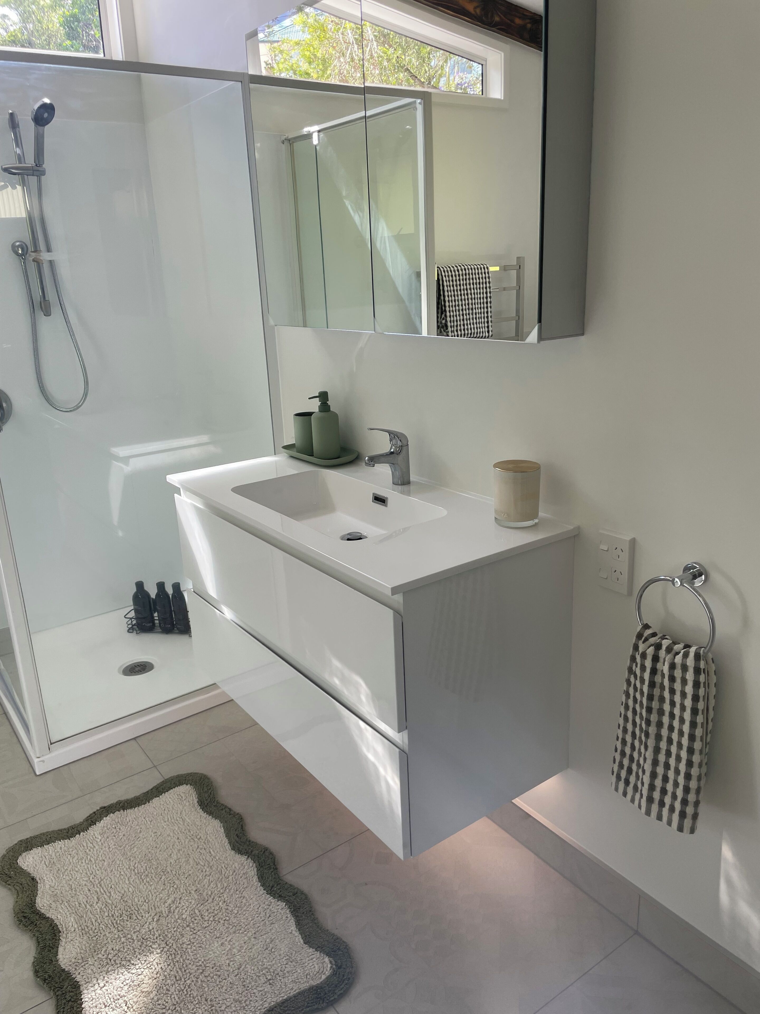 Une salle de bain moderne avec une douche à parois de verre, un lavabo blanc et un grand miroir.
