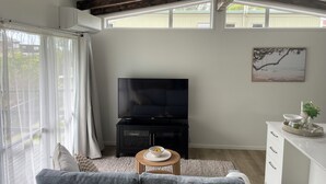 Una sala de estar moderna con una televisión de pantalla plana, un sofá gris, una mesa de centro de madera y un mueble blanco.