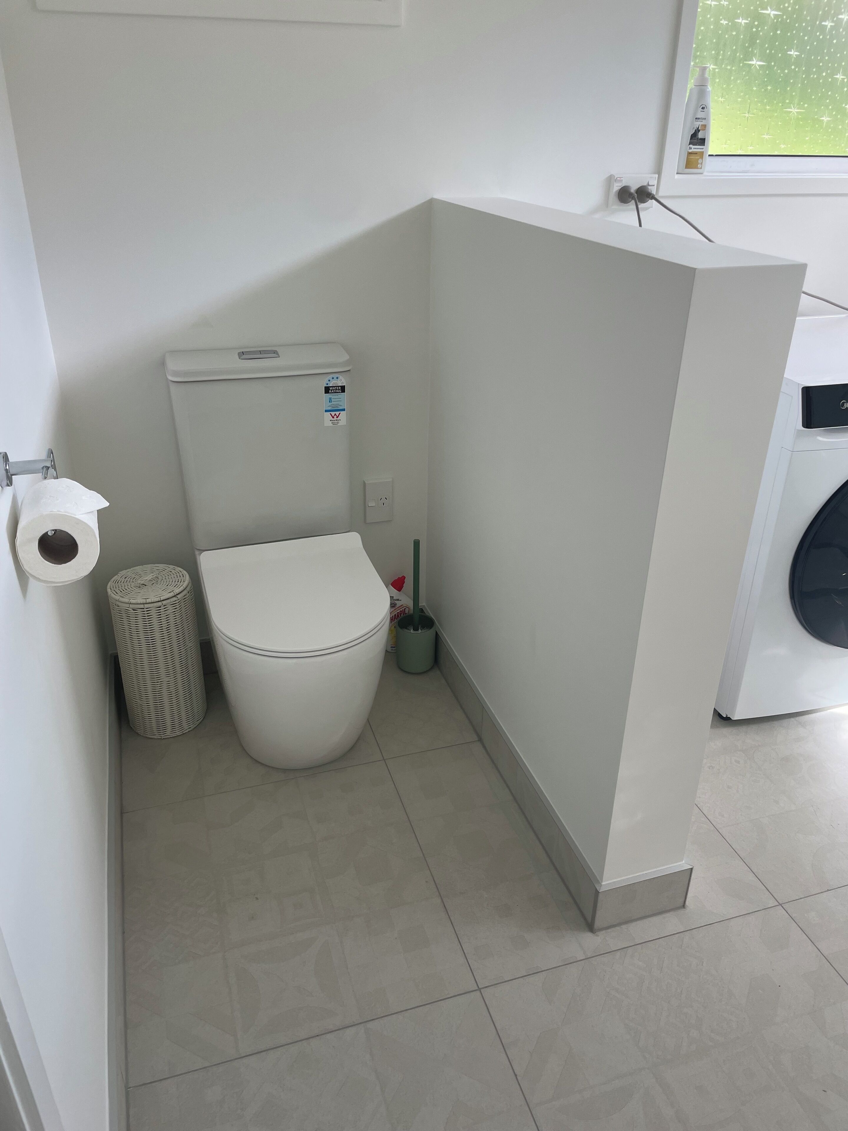 Une petite salle de bain propre, équipée de toilettes, d’une poubelle et d’un sèche-mains.
