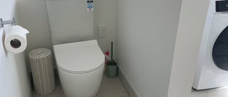 Une petite salle de bain propre, équipée de toilettes, d’une poubelle et d’un sèche-mains.