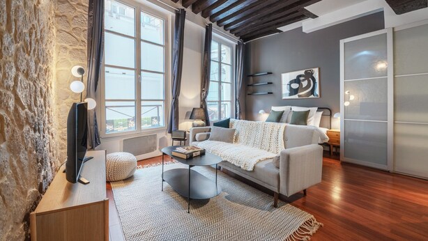A modern living room with a sofa, coffee table, and a TV on a wooden stand. - Blueground | Le Marais, near Seine River (Paris)