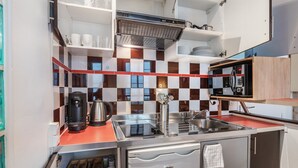 A compact kitchen with a coffee maker, kettle, and microwave. There are shelves with dishes and a small refrigerator. - Blueground | Le Marais, near Seine River (Paris)
