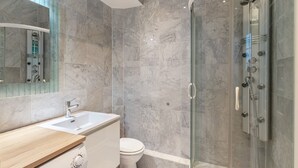 A modern bathroom with a marble-tiled shower, a glass-enclosed shower area, a white sink, and a toilet. - Blueground | Le Marais, near Seine River (Paris)