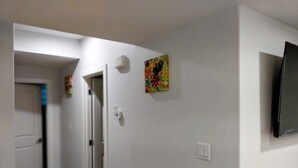 A hallway with white walls, a wooden floor, a door, and a mounted TV.