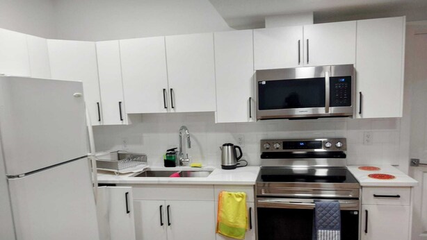 A modern kitchen with white cabinets, stainless steel appliances, and a wooden floor.